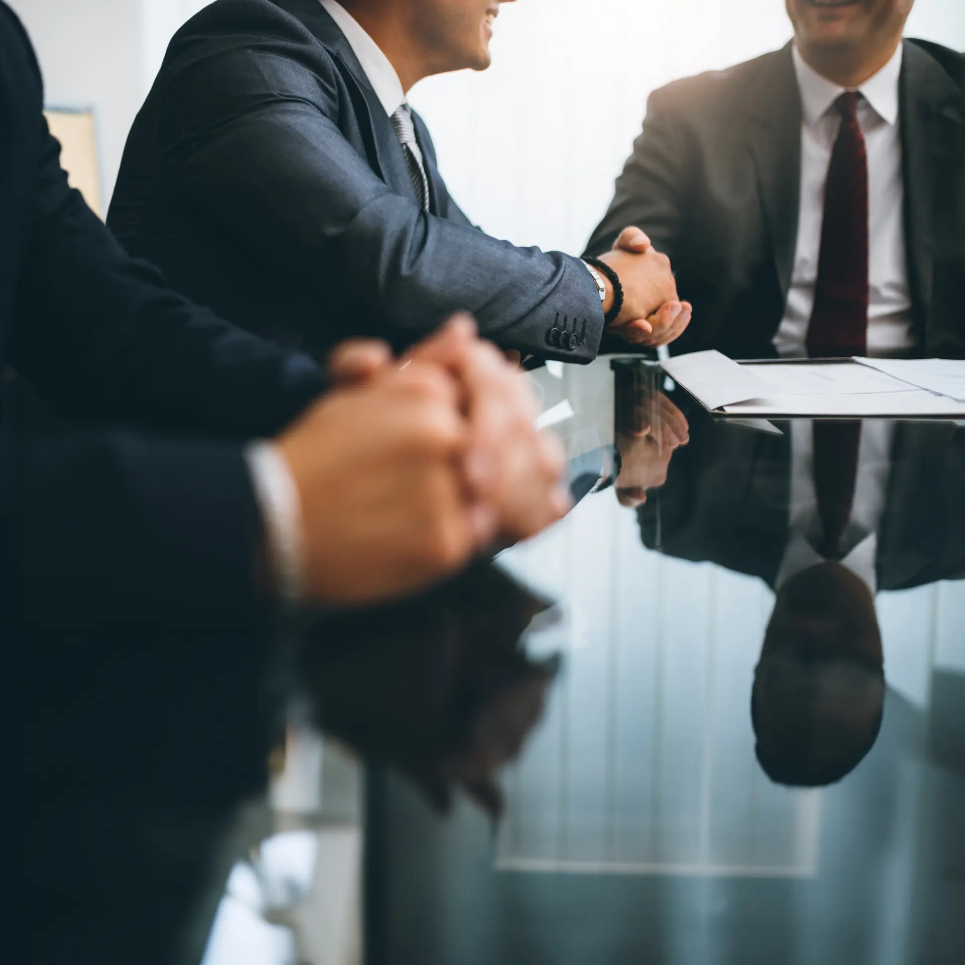 Professional business meeting with handshake over glass table, symbolizing successful merger and acquisition deals
